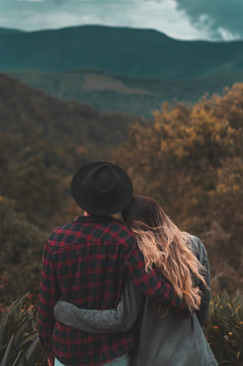A picture of a couple with their arms around each other looking at the mountains.