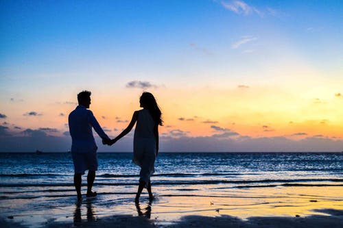 A soothing picture of a couple holding hands on a beach.